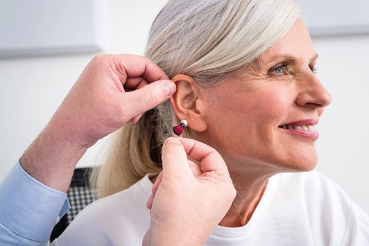 Ältere Frau bekommt ein modernes Hörgerät ins Ohr eingesetzt, Hörgeräteanpassung.